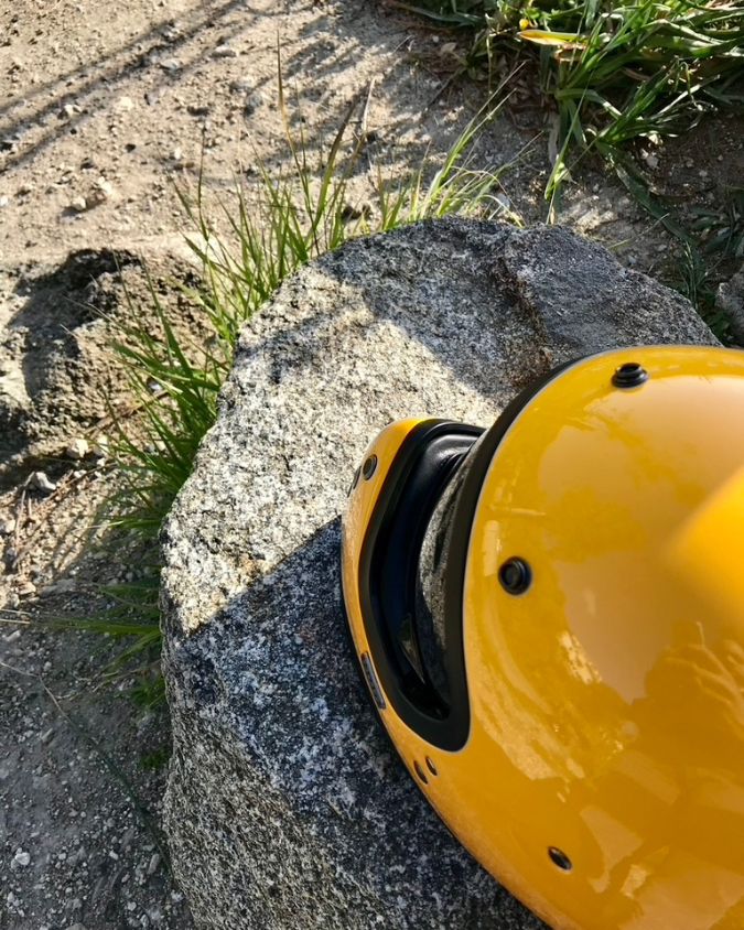 Foto del casco giallo di Andrea poggiato su una pietra e circondato da erbetta e terra. Rappresenta la fermezza della propria identità.
